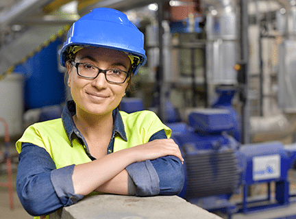 Mujer con ropa de alta visibilidad y casco en una fábrica sonriendo a la cámara.