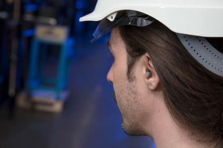 Primer plano operario de fábrica equipado con casco y tapones para los oídos para mayor seguridad.