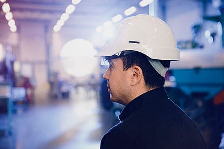 Ein Arbeiter trägt einen weißen Helm in einer blau beleuchteten Fabrikhalle.